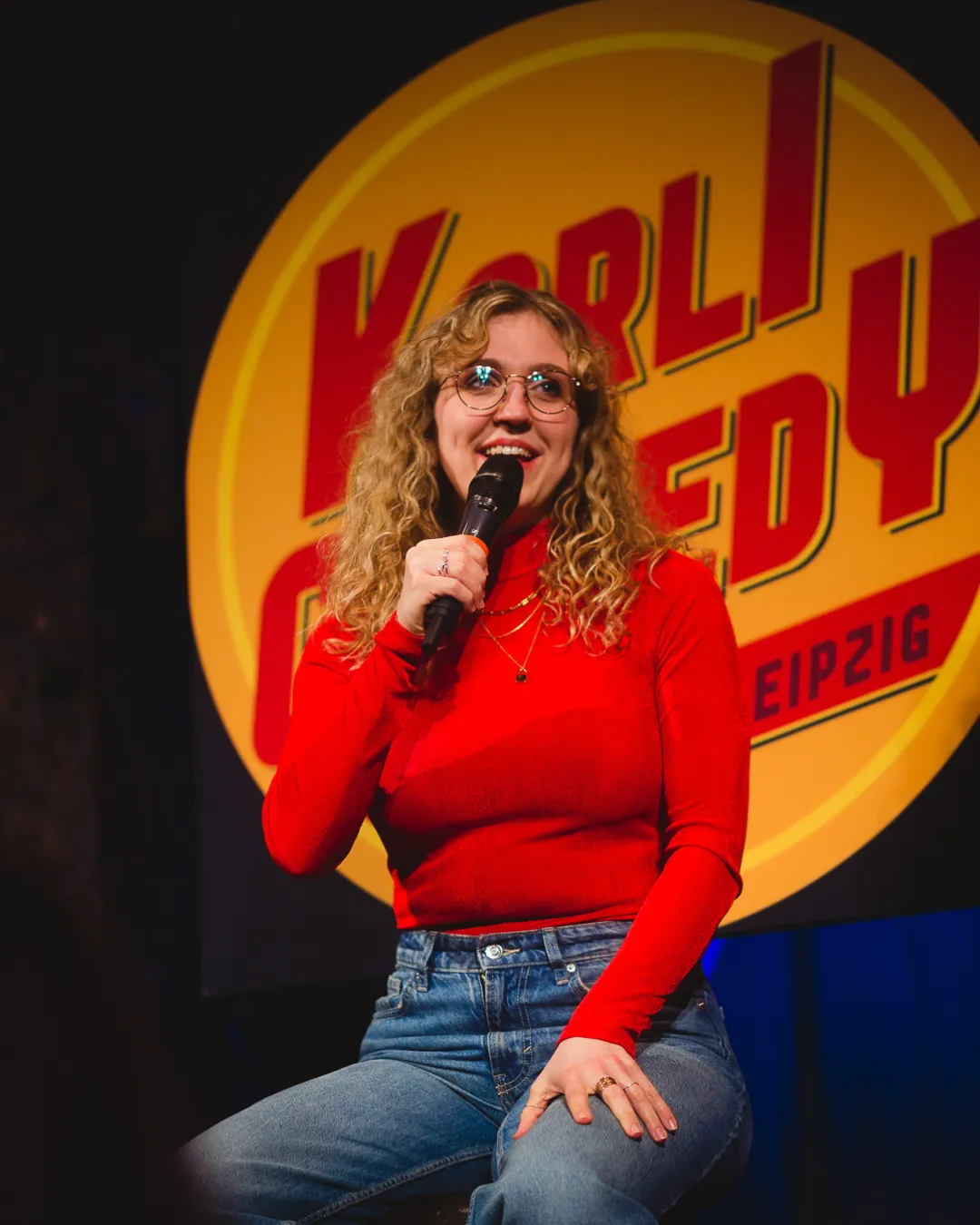 Comedian mit Mikrofon auf einem Barhocker auf der Bühne